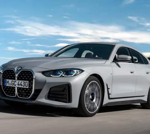 Eleganckie, szare BMW Gran Coupé sunie po drodze na tle błękitnego nieba z chmurami.