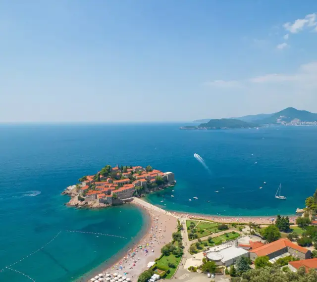 Sveti Stefan, perła Czarnogóry, idealne miejsce na wycieczki. Wyspa z czerwonymi dachami, plaża, turkusowe morze i góry w tle.