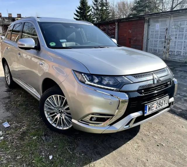 Srebrny Mitsubishi Outlander PHEV na tle garaży. Wiele osób szuka mitsubishi outlander opinie przed zakupem.