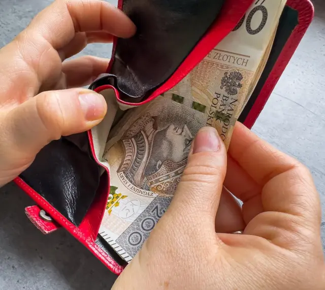 Ręce wkładają banknoty do czerwonego portfela. To może być 1000 zł na drugie dziecko, wsparcie dla rodziny.