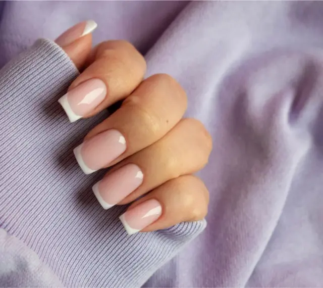 Dłoń z paznokciami w stylu french kolor, na tle lawendowej bluzy. Klasyka i elegancja.