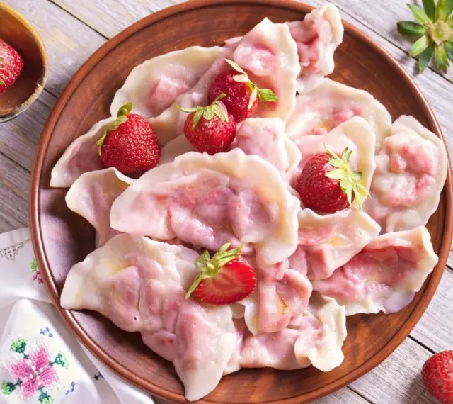 Pyszne pierogi z truskawkami, ozdobione świeżymi owocami, wyglądają apetycznie na glinianym talerzu.