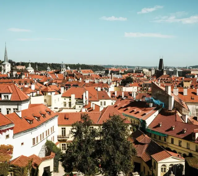 Widok na dachy Pragi, idealne miejsce na tani city break. W oddali wieże i kopuły.