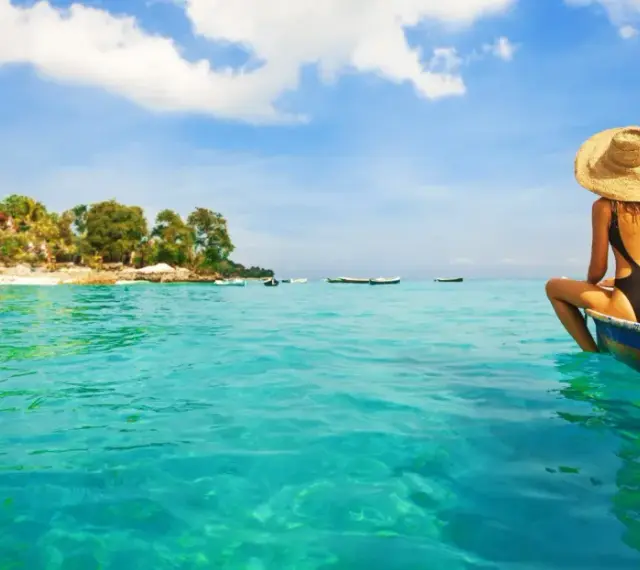 Kobieta w kapeluszu siedzi na łodzi, podziwiając turkusowe morze i tropikalne plaże na Bali.