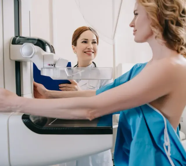 Kobieta przygotowuje się do mammografii, podczas gdy radiolog uśmiecha się wspierająco.