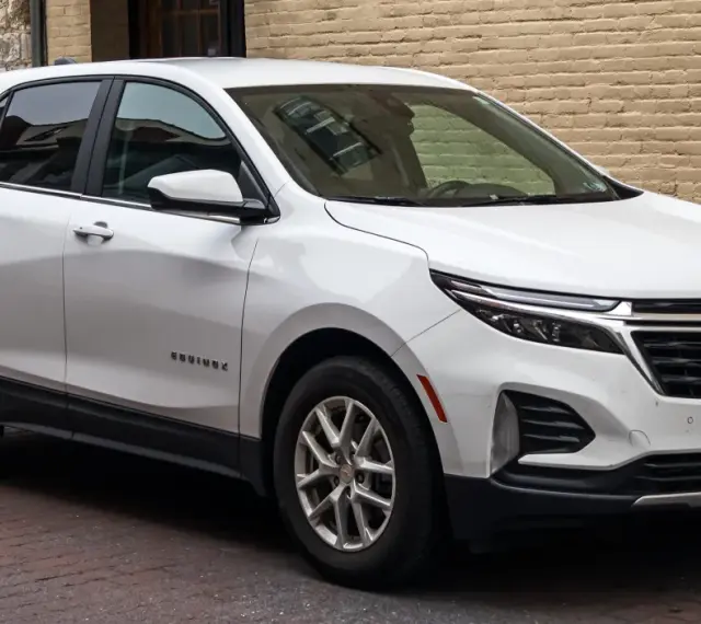Biały Chevrolet Equinox, wszechstronny chevrolet suv, zaparkowany na brukowanej ulicy przed ceglanym budynkiem.
