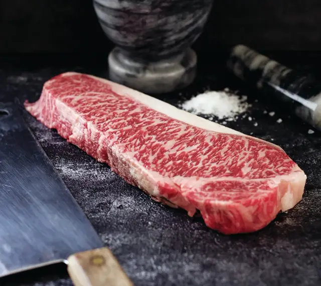 Wyjątkowy stek z krowy wagyu, gotowy do przygotowania. Obok nóż i moździerz z solą.