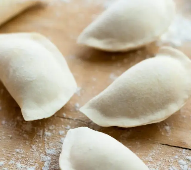 Surowe pierogi na drewnianej desce, przygotowane z ciasta na pierogi bez jajka.