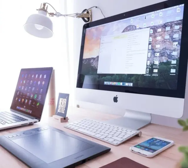 Biurko z iMac, laptopem, tabletem graficznym i telefonem. Na ekranie komputera widać okno programu Adobe Dreamweaver, gotowe do pracy nad stroną.