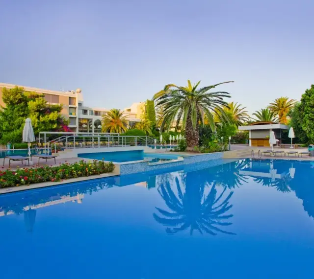 Basen hotelowy z palmami i kwitnącymi kwiatami, idealne miejsce na relaks przy Caravia Beach Kos.