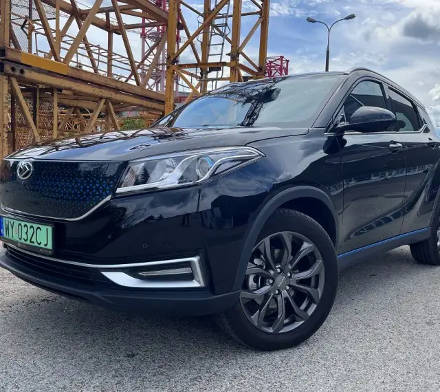 Czarny, lśniący SUV, jeden z chińskich samochodów elektrycznych, zaparkowany obok żółtej konstrukcji budowlanej.