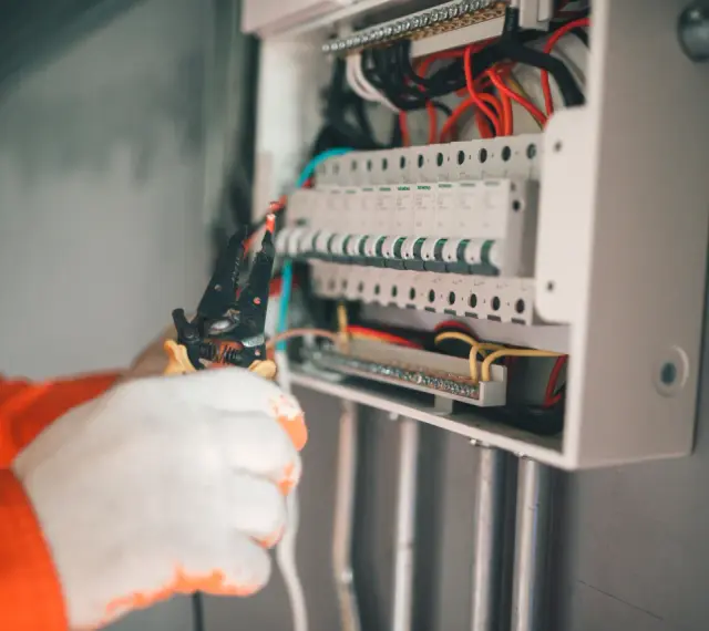 Elektryk w białych rękawiczkach montuje zabezpieczenie przedlicznikowe w skrzynce z bezpiecznikami.