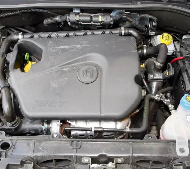 Silnik 1.4 z Fiata Grande Punto. Widoczny plastikowy kolektor, akumulator i zbiornik płynu chłodniczego.