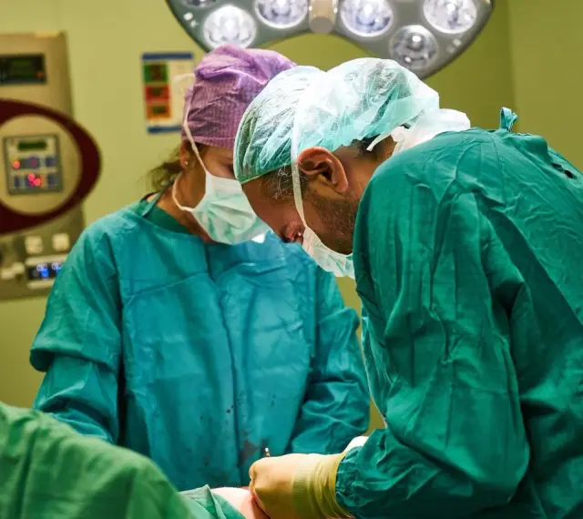 Chirurdzy w maseczkach i czepkach przygotowują się do operacji. Narkoza już działa, pacjent jest bezpieczny.