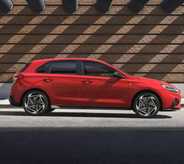 Czerwony Hyundai i30 stoi na tle ceglanej ściany z ciekawymi cieniami.