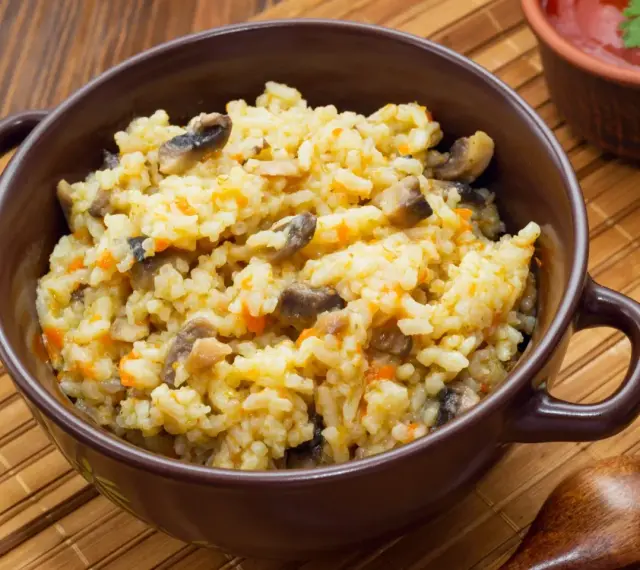 Kremowe risotto z grzybami i marchewką w brązowej misce, obok drewniana łyżka.