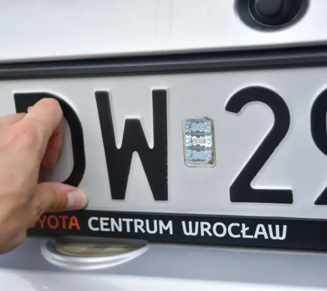 Dłoń zasłania literę "D" na tablicy rejestracyjnej DW 29. Widoczny hologram i napis "TOYOTA CENTRUM WROCŁAW".
