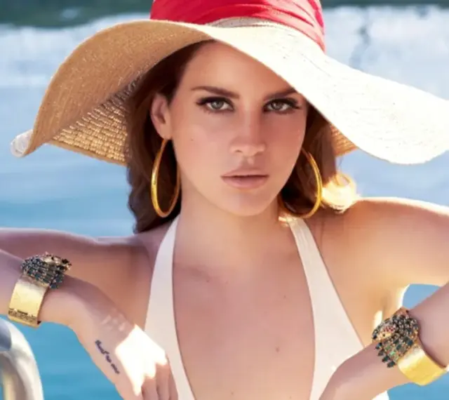 Lana Del Rey, wokalistka, w letnim kapeluszu i biżuterii, relaksuje się przy basenie.