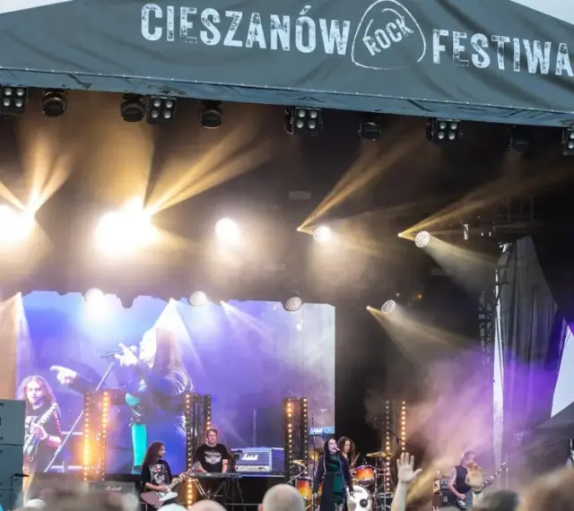 Zespół gra na scenie podczas Cieszanów Rock Festiwal. W tle wielki ekran z wizerunkiem wokalistki i reflektory.