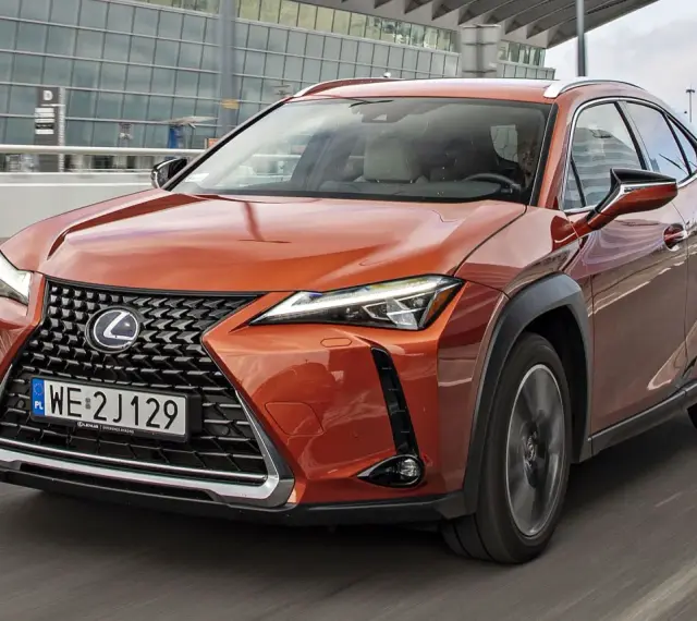 Pomarańczowy Lexus UX 250h w ruchu miejskim, z nowoczesnym grillem i reflektorami LED.