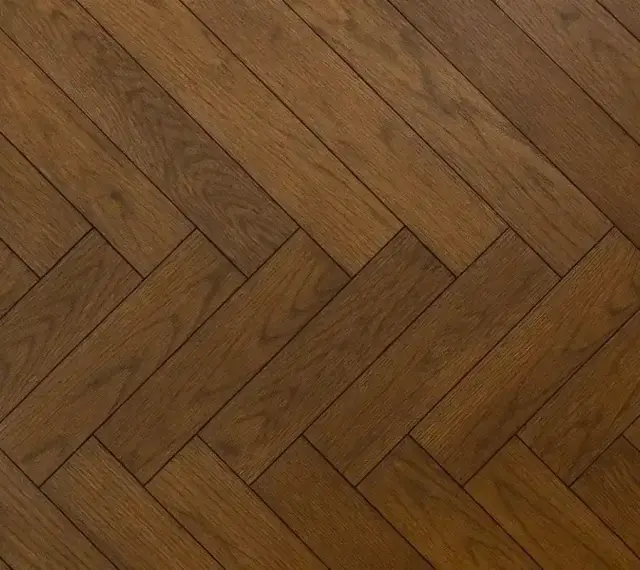 Vacker fiskbensparkett i mörkt trä, redo att slipa för att återfå sin glans.