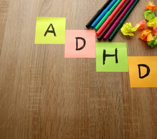 Kolorowe karteczki z literami "A", "D", "H", "D" układają się w napis ADHD. Obok leżą pisaki i pomięte papierki, jakby ktoś próbował znaleźć rozwiązanie, może z pomocą leku Elvanse.