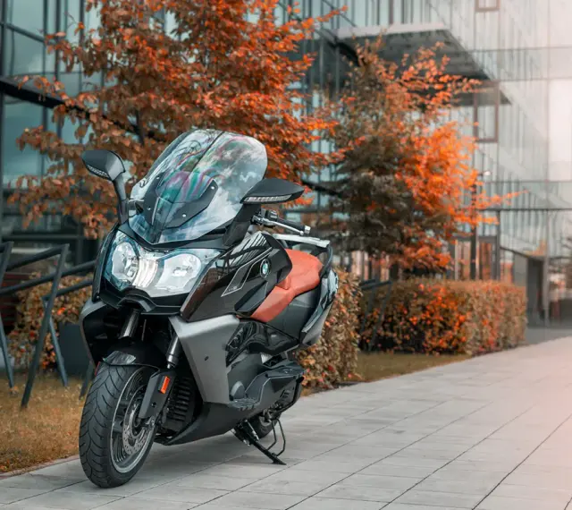 Skuter BMW C650 GT z brązowym siedzeniem na tle nowoczesnego budynku i jesiennych drzew. Dane techniczne tego modelu są imponujące.