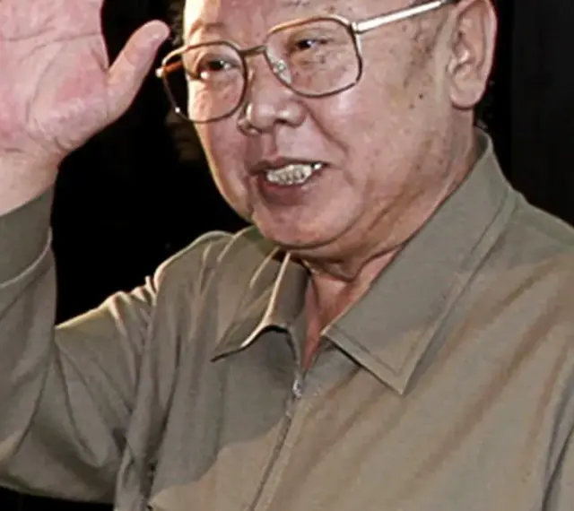 Kim Jong Il w okularach, machający ręką.
