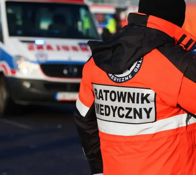 Ratownik medyczny w pomarańczowej kurtce z napisem "RATOWNIK MEDYCZNY" obok karetki. Zastanawiasz się, ile zarabia ratownik medyczny?