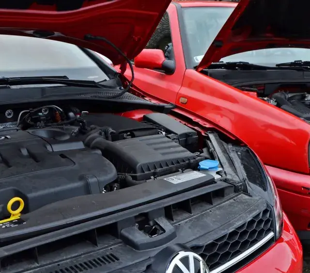 Dwa czerwone Volkswageny z otwartymi maskami. Nowszy model z silnikiem TDI obok starszego, gdzie widać stary diesel.