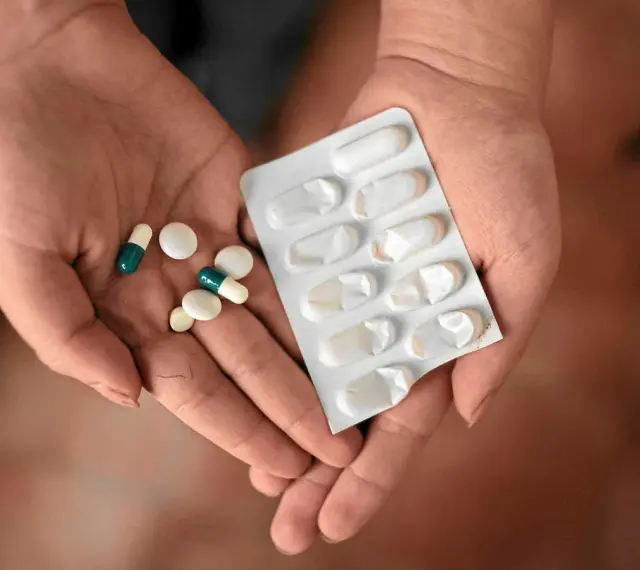Dłonie trzymające tabletki i blister. Wśród nich są leki, które mogą być inhibitorami pompy protonowej, pomagając w leczeniu dolegliwości żołądkowych.