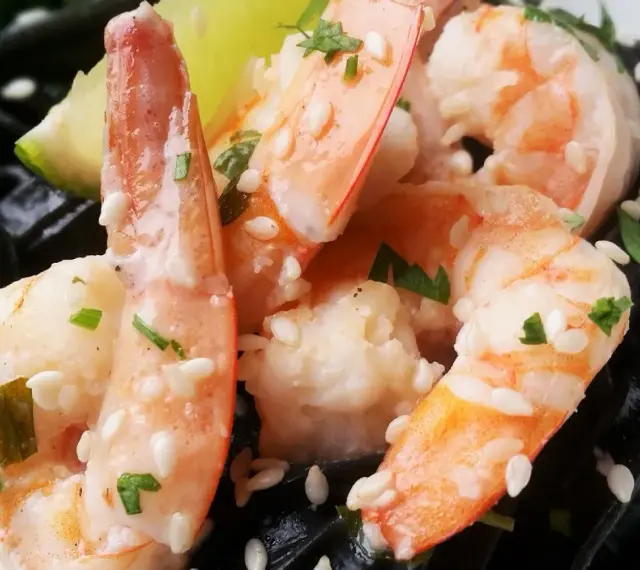 Krewetki z czarnym makaronem, posypane sezamem i natką pietruszki, z kawałkiem limonki.