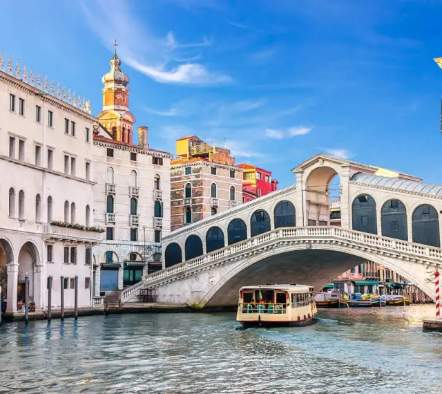Venezia, il Canal Grande con il Ponte di Rialto e il Fondaco dei Tedeschi sullo sfondo. Una motonave naviga sull'acqua.