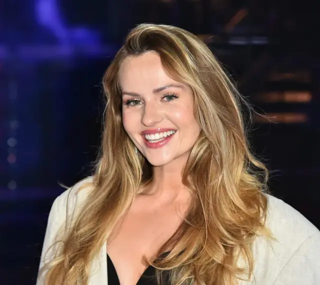 Uśmiechnięta Żaneta Rosińska, której wiek dodaje jej uroku, w białej marynarce i czarnej kreacji.