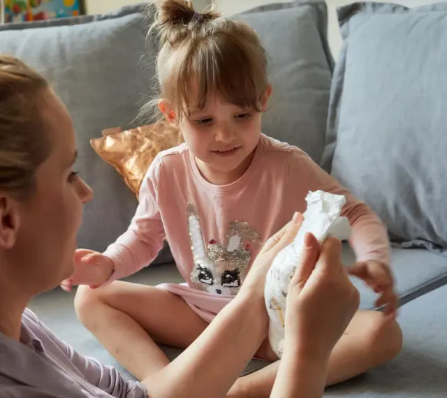 Mama pokazuje córce pieluchę, symbolizując etap, kiedy dziecko przestaje nosić pieluchy.