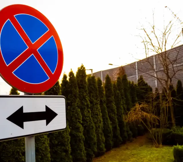 Znak zakaz parkowania z tabliczką wskazującą kierunki.