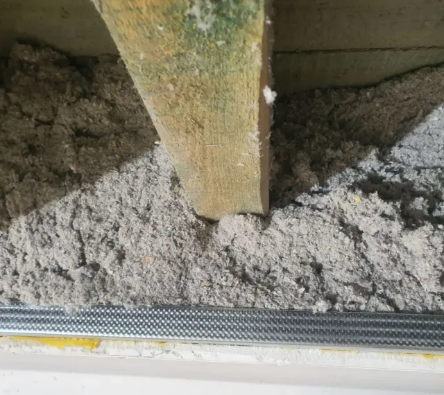 Izolacja z celulozy wypełnia przestrzeń między drewnianymi belkami stropowymi, tworząc warstwę termoizolacyjną.