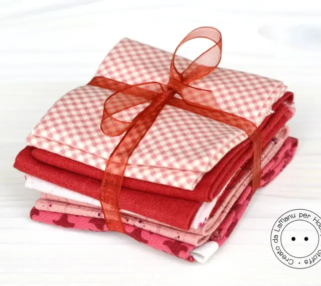 Fazzoletti di stoffa rossi e rosa, con fantasie a quadretti e cuoricini, legati da un nastro. Perfetti per un progetto di cucito creativo.