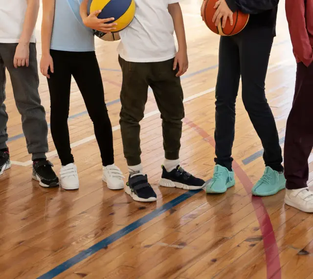 Dzieci na sali gimnastycznej, zastanawiające się, jakie buty na WF do szkoły wybrać. Różne modele sportowego obuwia na drewnianej podłodze.