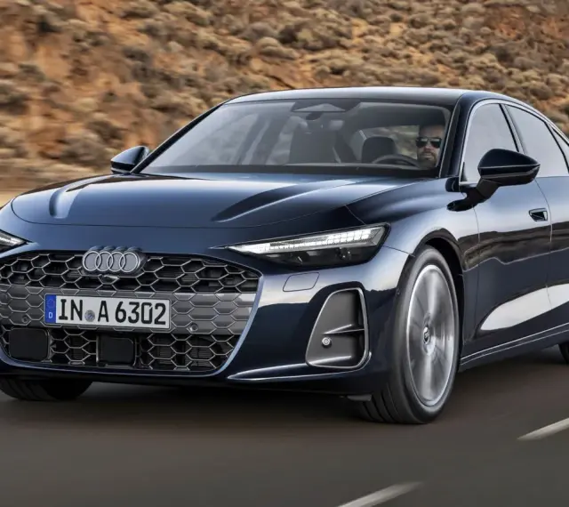 Elegancki, ciemnogranatowy Audi A6 sunie po drodze, z kierowcą w okularach za kierownicą.