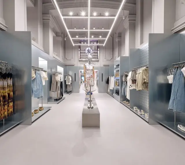 Nowoczesne wnętrze sklepu Bershka z wieszakami pełnymi ubrań i manekinem w centrum.