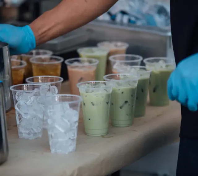 Przygotowanie do zrobienia kulek do bubble tea: ręce w niebieskich rękawiczkach, dzbanki, kubki z lodem i gotowe napoje.
