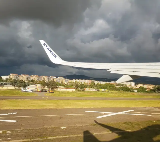 Skrzydło samolotu Ryanair nad lotniskiem, ciemne chmury na niebie.