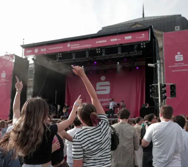 Menschen jubeln bei einem Open-Air-Konzert vor einer Bühne mit Sparkassen-Logo.