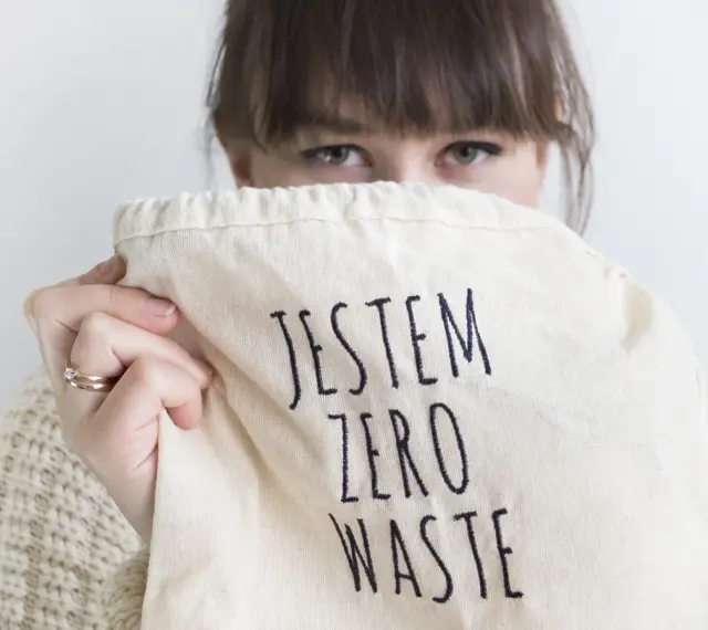 Sylwia Majcher, z uśmiechem ukrytym za torbą z napisem "Jestem Zero Waste", pokazuje swoje zaangażowanie w ekologię.