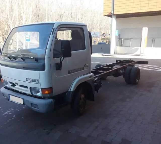 Biały Nissan Cabstar bez zabudowy, z widocznym gołym podwoziem i podwójnymi tylnymi kołami, stoi na kostce brukowej.