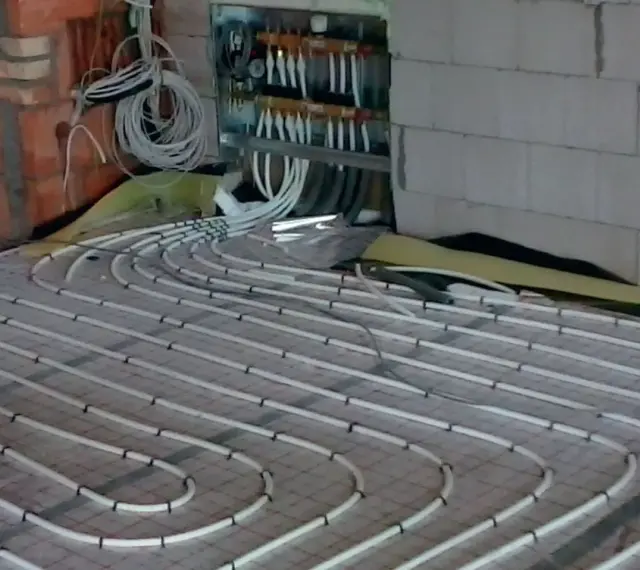 Instalacja ogrzewania podłogowego. Rury ułożone na siatce, podłączone do rozdzielacza. To rozwiązanie obniża koszt ogrzewania.