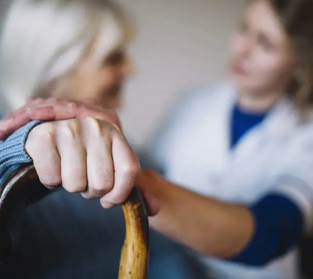 Opiekunka wspiera starszą panią, która trzyma laskę. Zastanawiasz się, ile kosztuje opiekunka z mops?