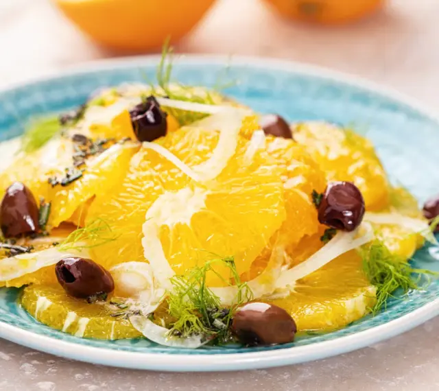 Erfrischender orangensalat sizilianisch mit Fenchel und dunklen Oliven auf einem blauen Teller.