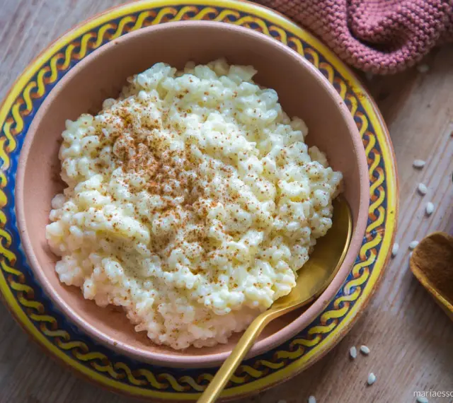 Cremiger Milchreis, bestreut mit Zimt, wartet in einer Schale auf sein Milchreis Rezept. Daneben liegen Reiskörner und Zimtstangen.